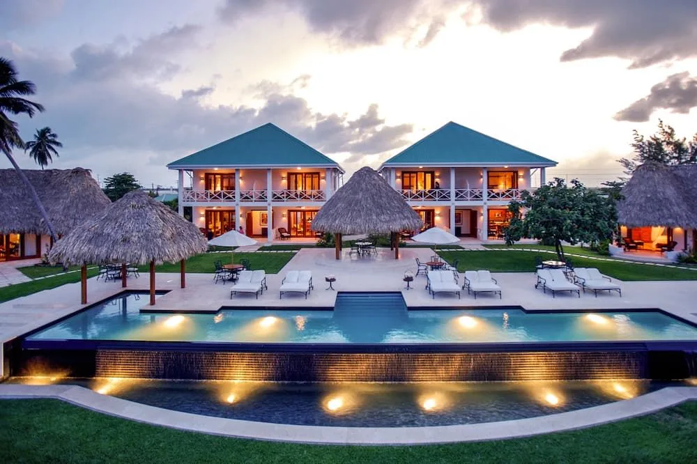 An illuminated tiered swimming pool and thatched palapas front two-story villas at a tropical Belize resort at dusk.