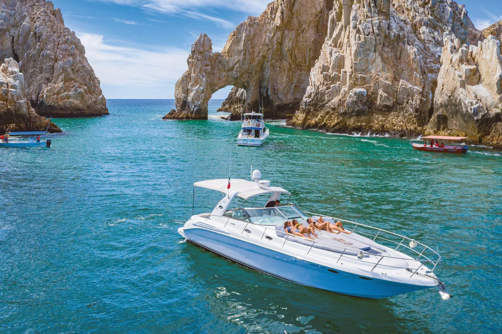 Sunbathers relax on a white yacht cruising turquoise waters near the iconic El Arco rock formation in Los Cabos, Mexico.