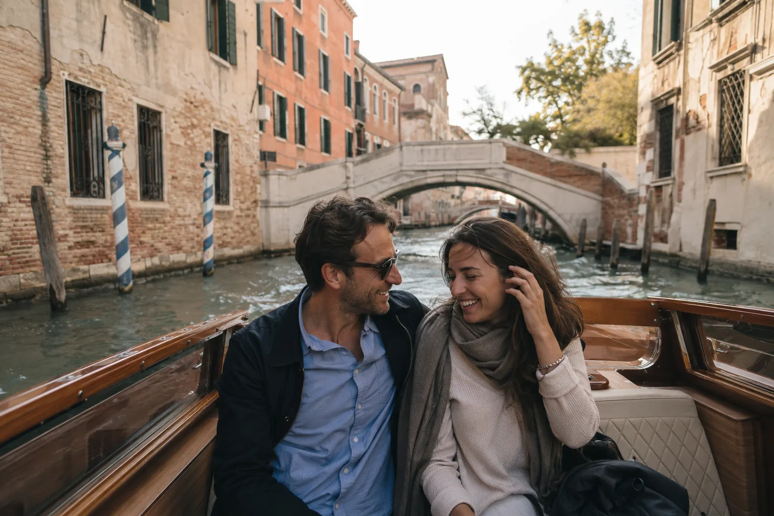 A smiling couple sits together in a wooden boat cruising along a scenic canal in Venice, Italy.