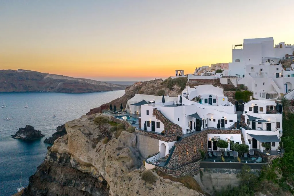 Whitewashed cliffside villas and terraces overlook the caldera at sunset in Santorini, Greece.