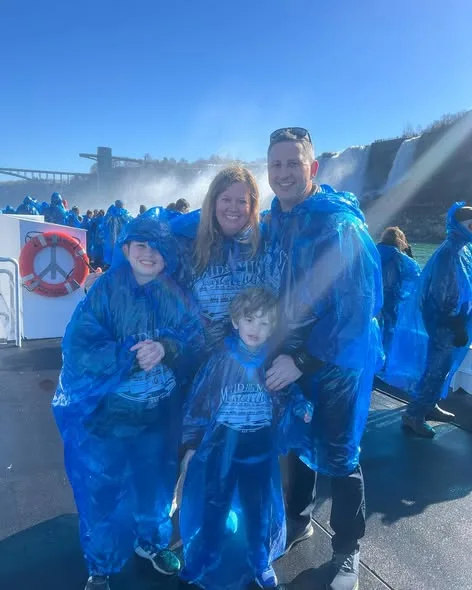A smiling family wearing blue ponchos stands on a tour boat deck in front of Niagara Falls.