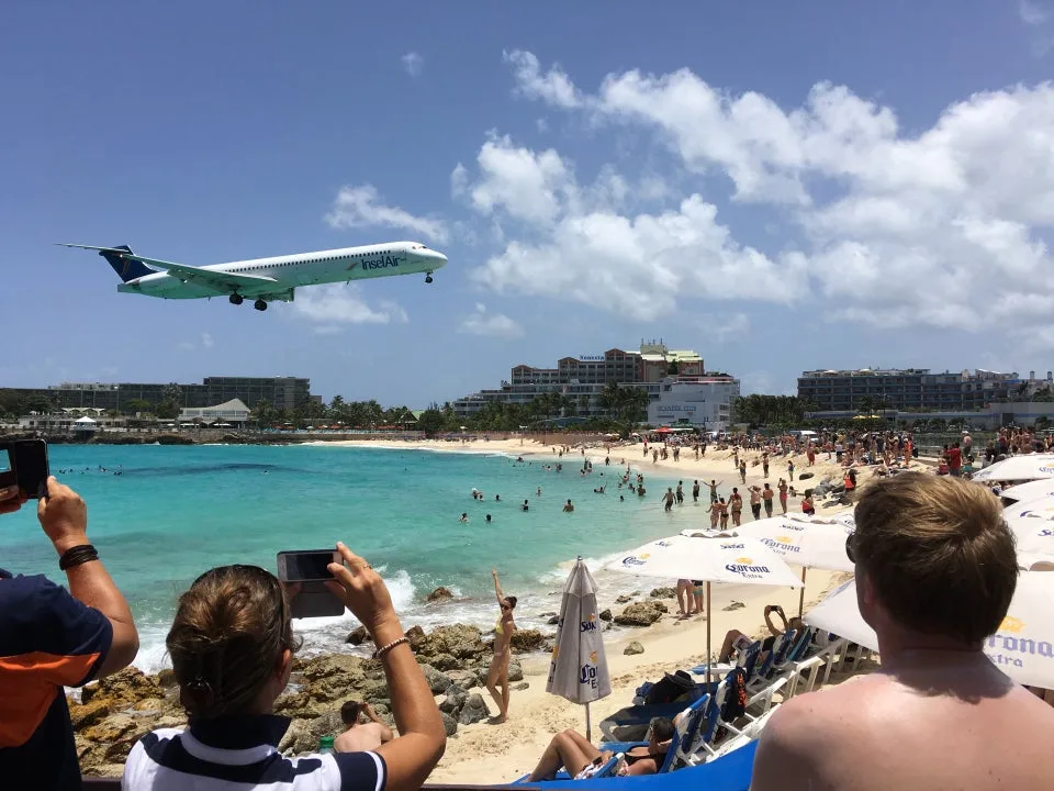 A commercial airplane descends low over sunbathers and turquoise waters at Maho Beach in Sint Maarten.