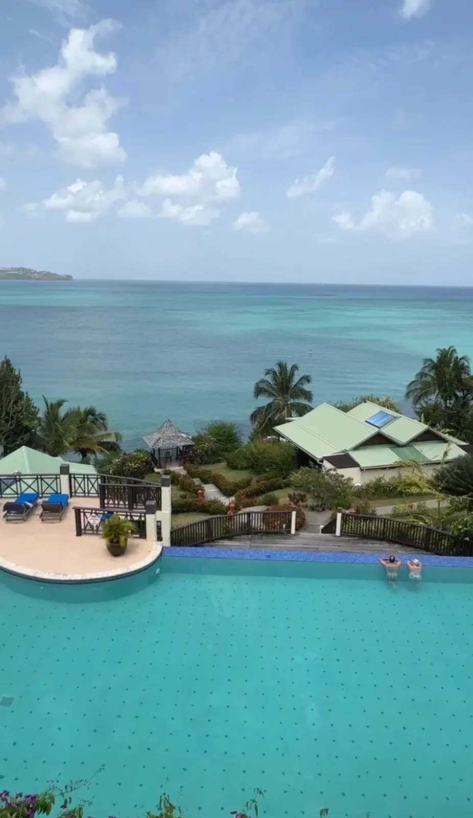 An infinity swimming pool overlooks tropical resort villas, lush palm trees, and the turquoise Caribbean Sea in Saint Lucia.