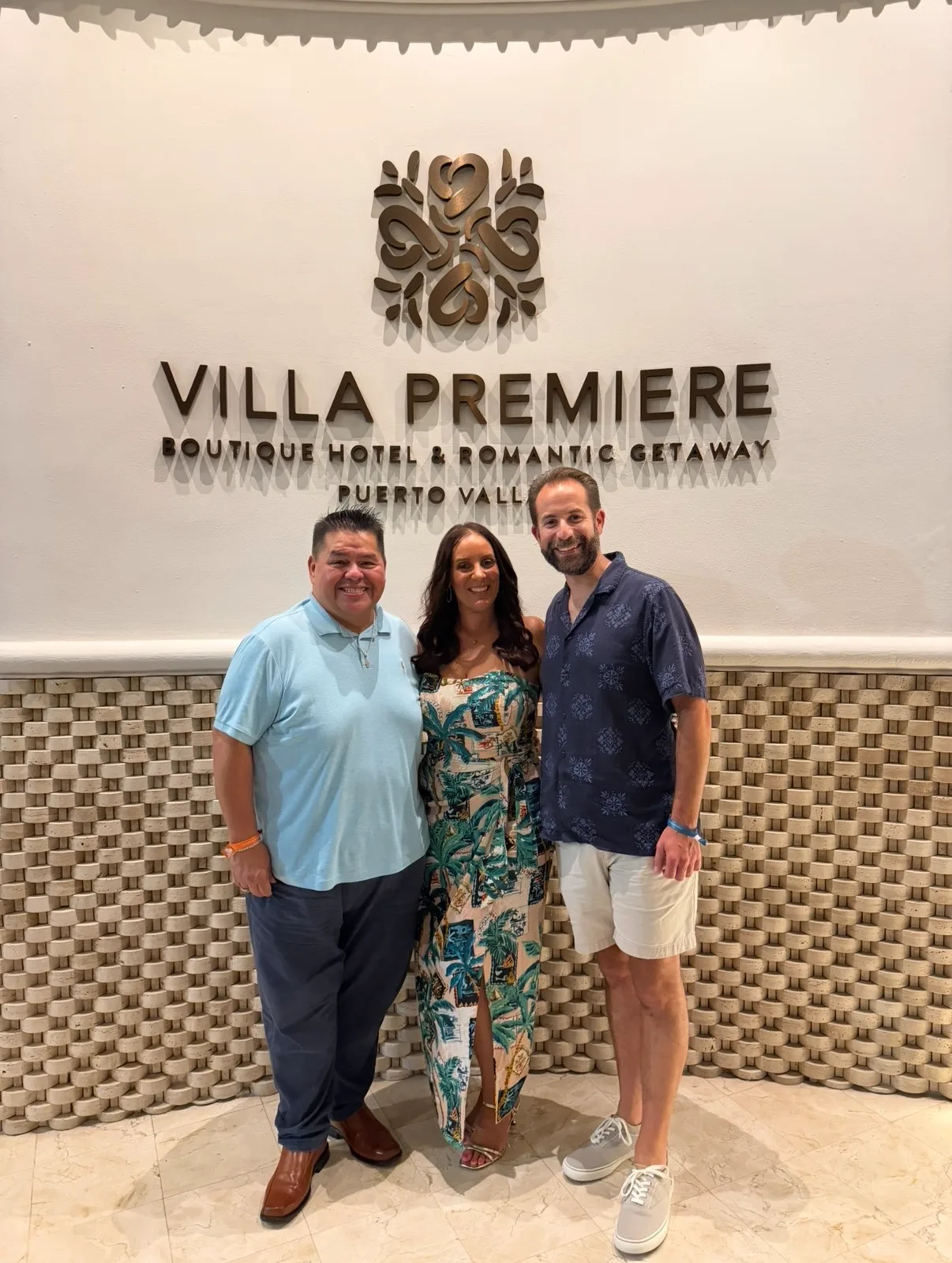 Three guests smile together in front of the lobby sign at Villa Premiere Boutique Hotel in Puerto Vallarta.