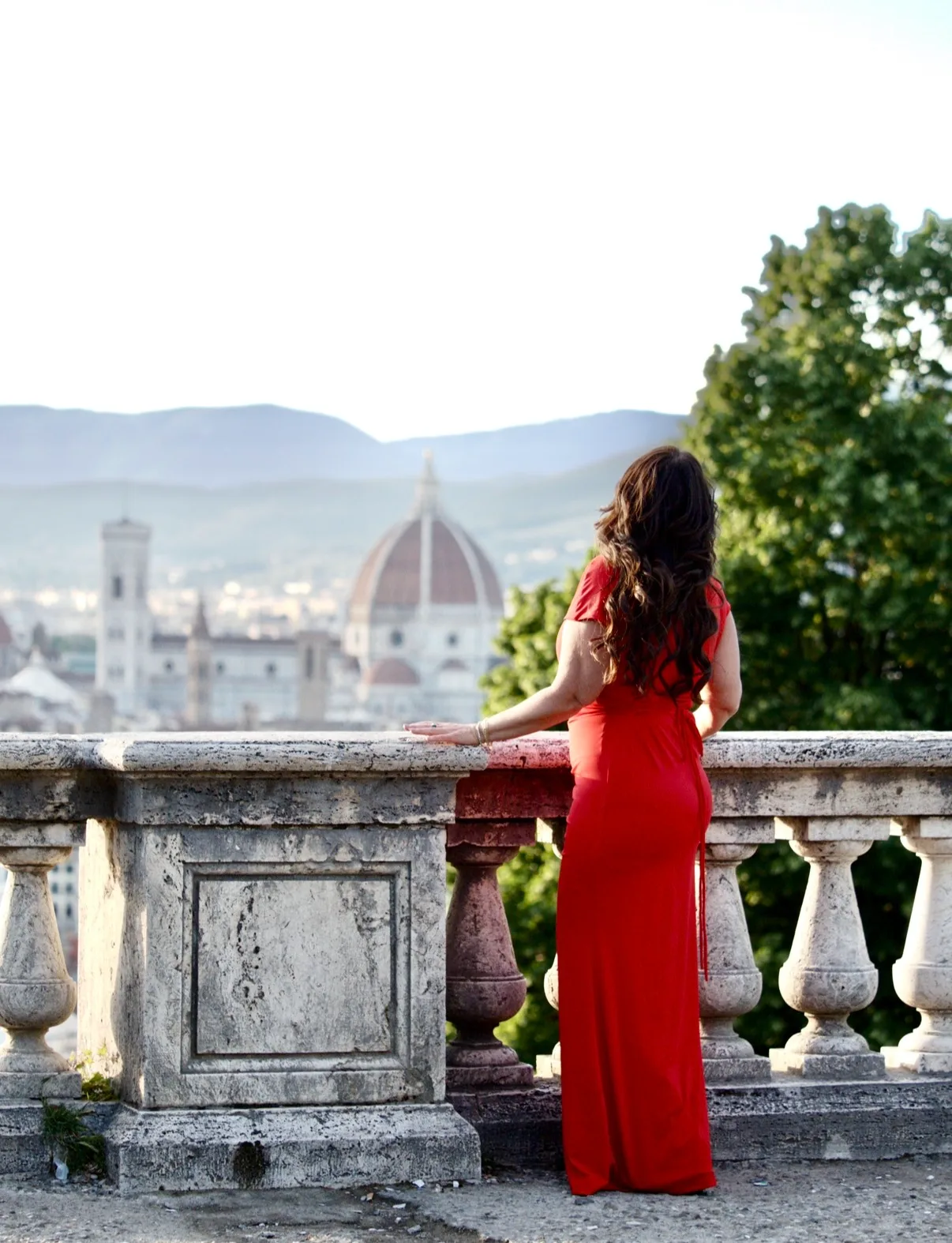 A woman in a red dress stands at a stone balustrade overlooking the Florence Cathedral and cityscape in Italy.