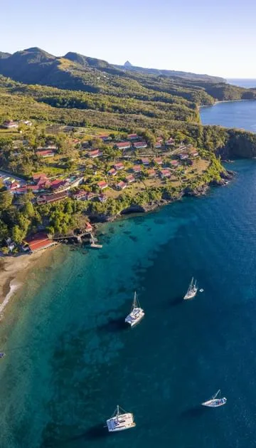 Red-roofed cottages cluster on a lush hillside above boats anchored in the clear turquoise waters of Saint Lucia.