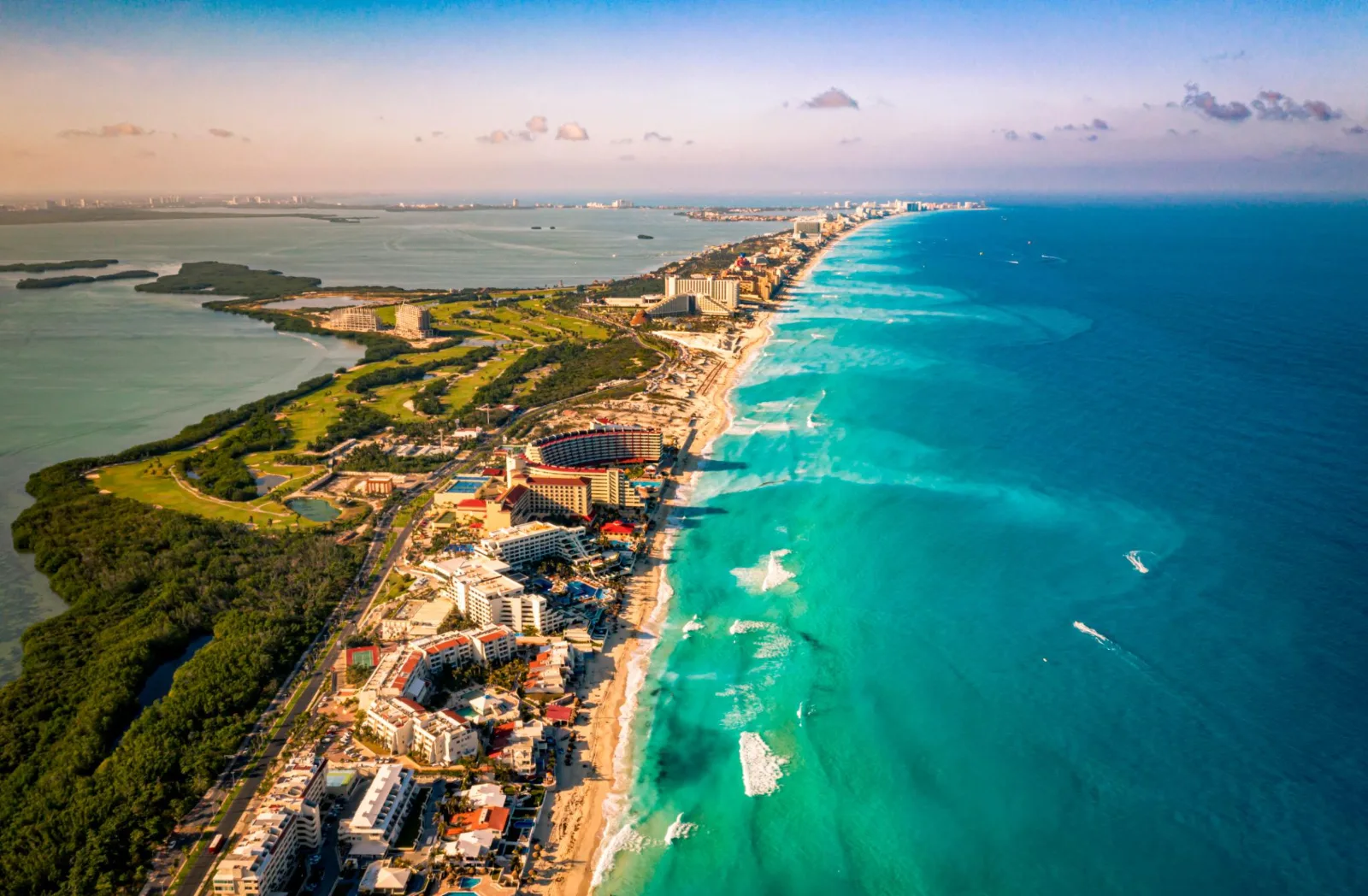 Coastal resorts and sandy beaches line a narrow strip between turquoise ocean waters and a lagoon in Cancún, Mexico.