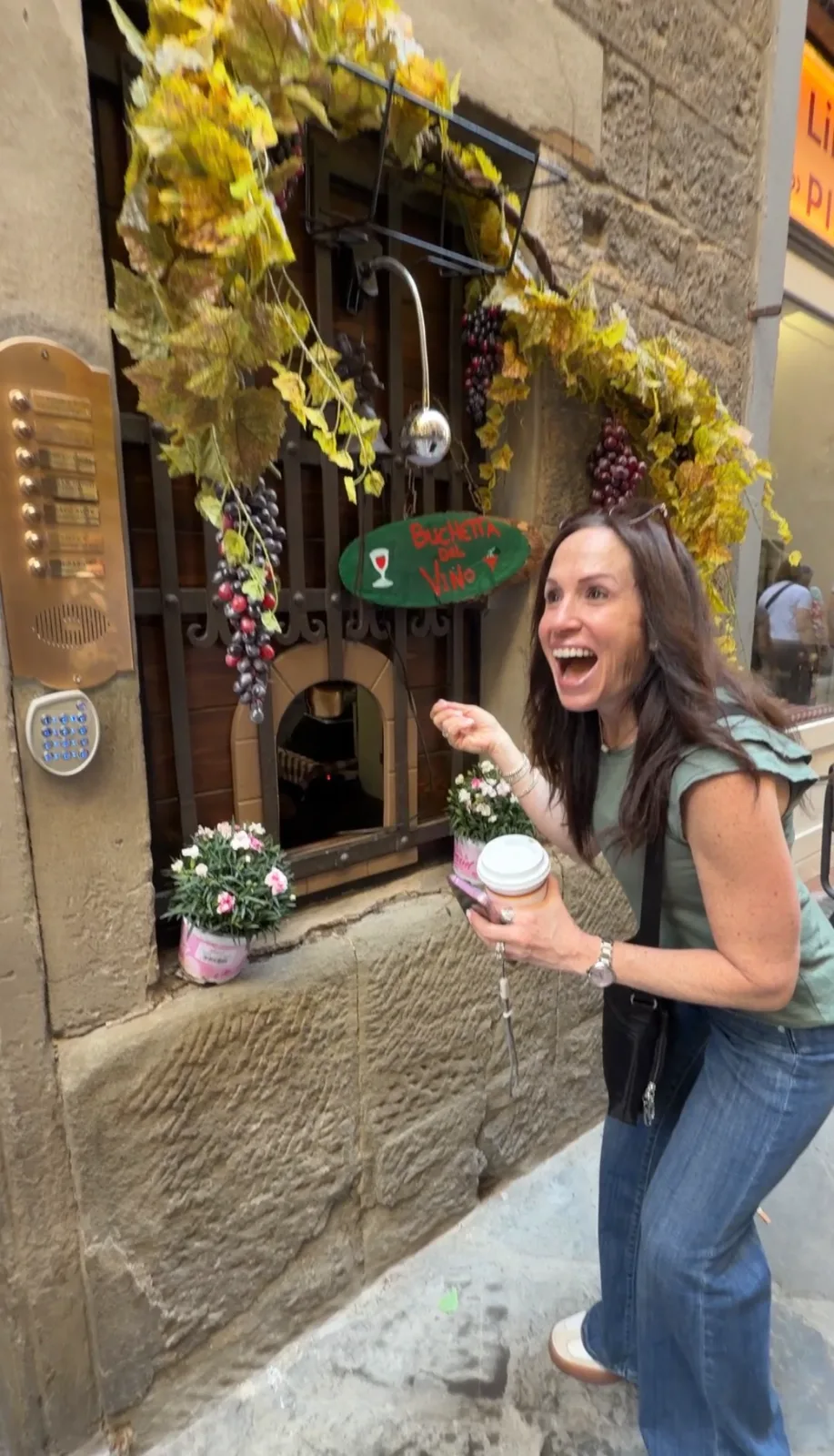 A joyful woman reacts outside a decorated historic wine window on a stone street in Florence.