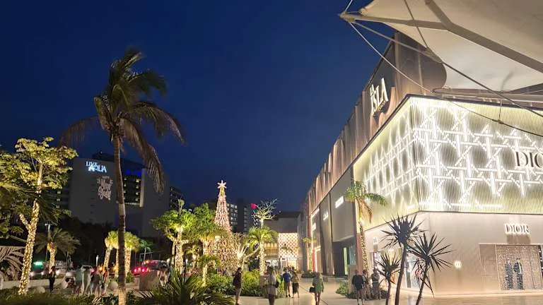 Illuminated luxury storefronts and palm trees line an outdoor promenade at La Isla Shopping Village at night in Cancun.