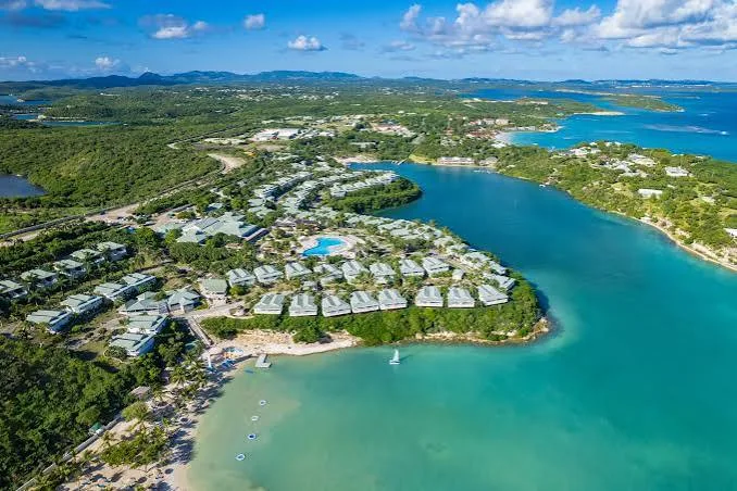 White villa suites at a beachfront resort extend along lush green headlands surrounded by turquoise ocean bays in Antigua.