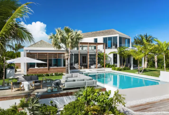 A modern two-story white villa features a swimming pool and furnished sun terrace, surrounded by palm trees under a blue sky.