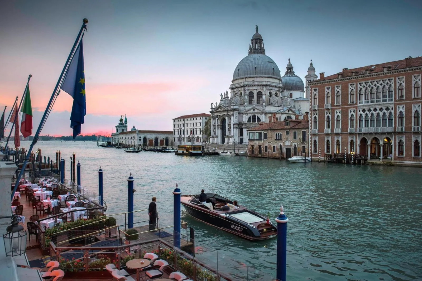 A water taxi arrives at a canal-side restaurant terrace overlooking the Basilica di Santa Maria della Salute in Venice.