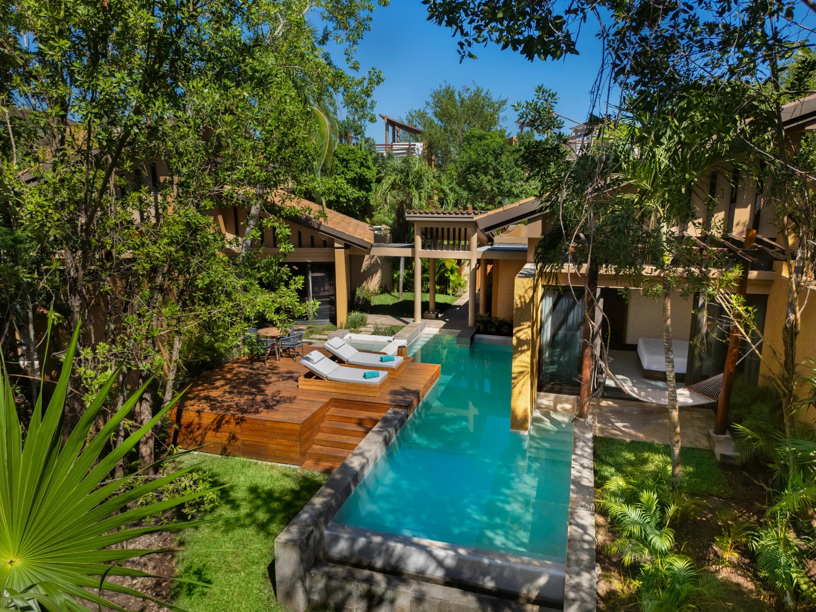 A private swimming pool and wooden sundeck bordered by lush tropical foliage beside contemporary villa suites in Riviera Maya, Mexico.