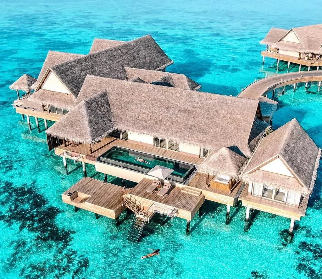 Thatched-roof overwater villas with a private pool and sun deck sit over a turquoise lagoon in the Maldives.