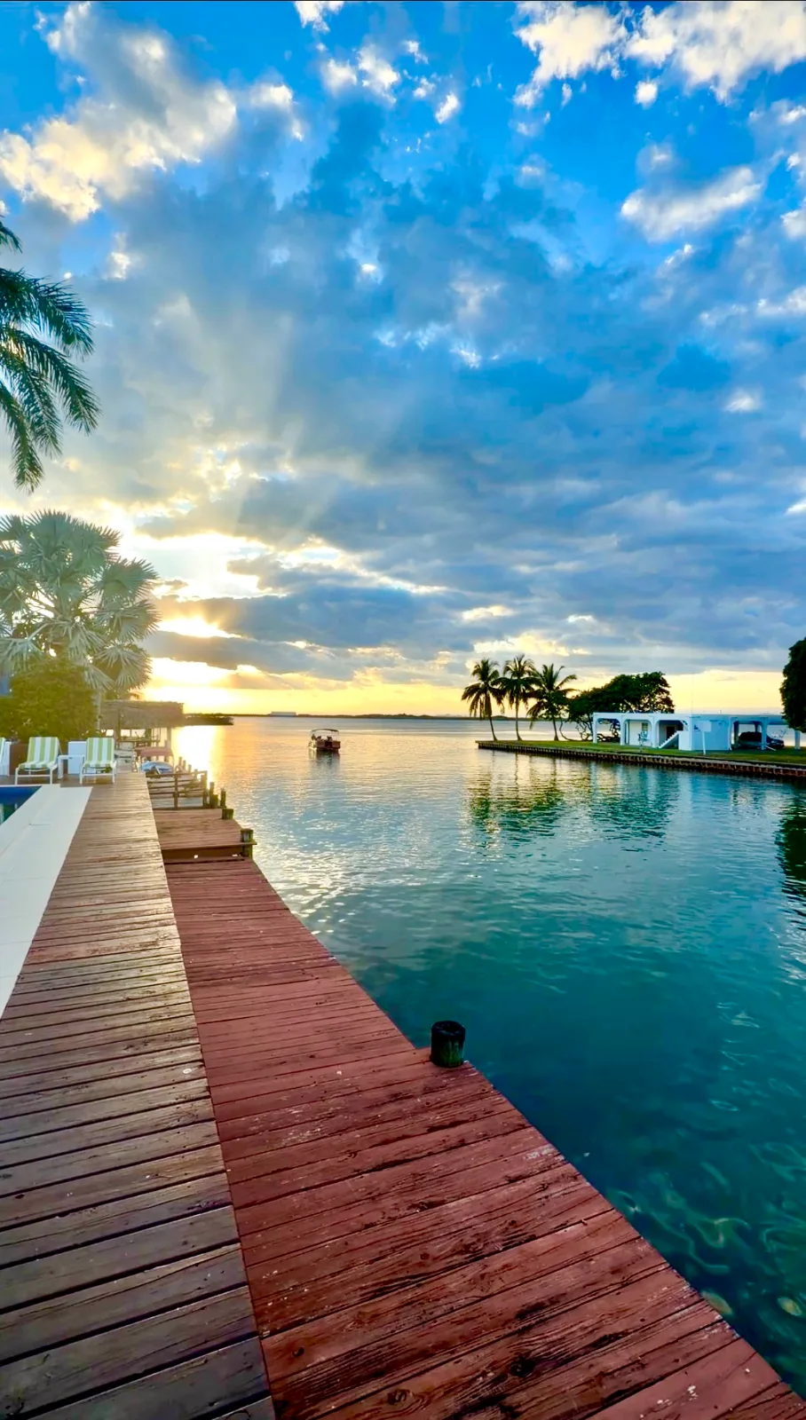 A wooden dock stretches along calm turquoise water toward a setting sun behind clouds in Belize.