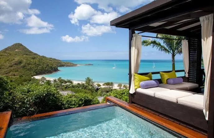 A private plunge pool and shaded daybed cabana overlook a turquoise bay and green hills in Antigua.