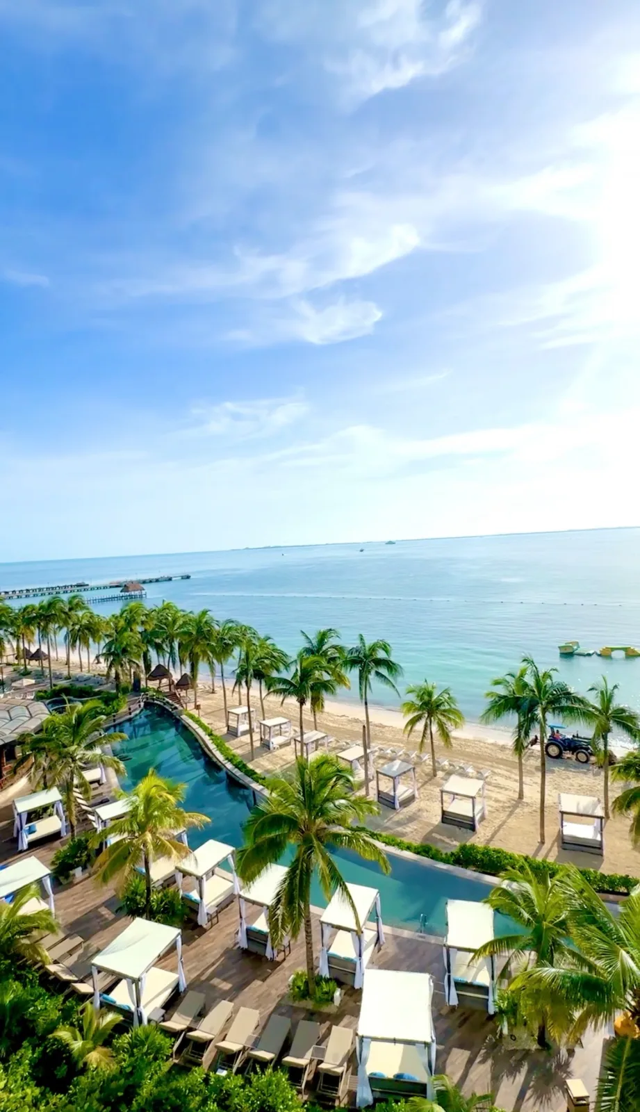 White cabanas and swimming pools line a palm-fringed beachfront overlooking the turquoise sea in Cancún, Mexico.