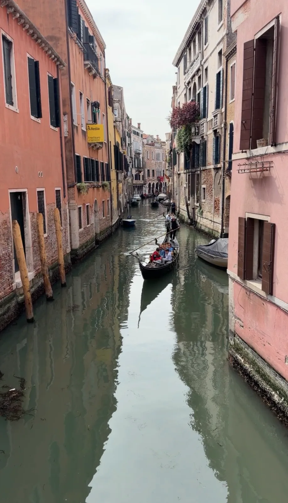 A gondolier navigates passengers down a narrow canal flanked by colorful historic buildings in Venice, Italy.